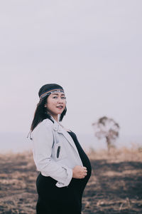 Young woman standing on field against sky