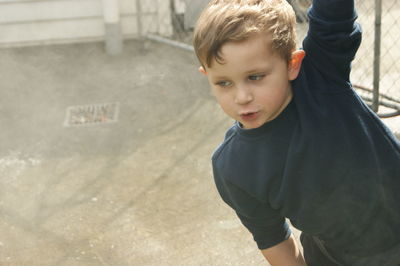 Boy with arm raised looking down while standing outdoors