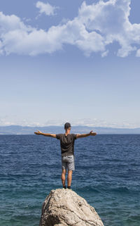 Rear view of man standing by sea against sky