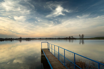 A bridge with a handrail on the lake, horizon and white clouds on a blue sky