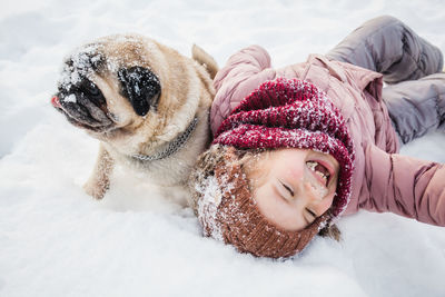 Cheerful girl with dog lying on snowy land