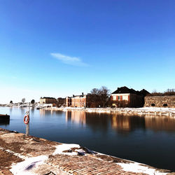 Buildings by lake against blue sky