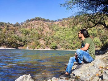 Full length of man sitting on rock against trees