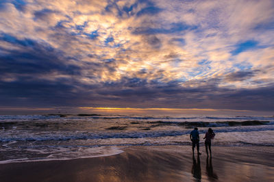 People standing on beach against sky during sunset