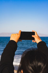 Midsection of person photographing sea against sky