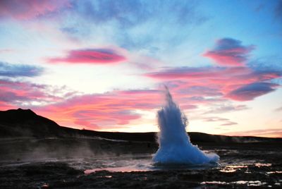 Scenic view of water splashing geyser against sunset sky