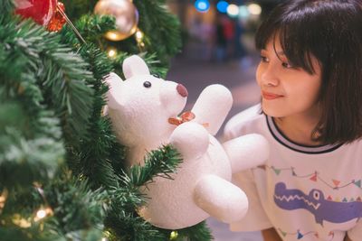 Young woman looking at stuffed toy hanging from christmas tree