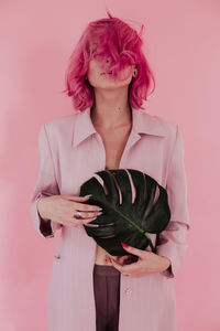 Young woman with dyed hair holding leaf while standing against colored background