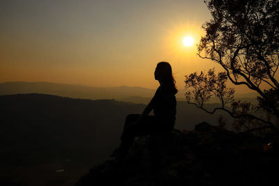 Silhouette woman sitting on rock against sky during sunset