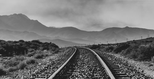 Railroad tracks leading towards mountains against sky