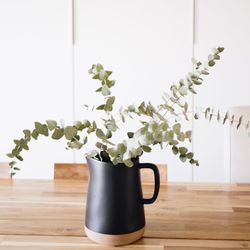 Eucalyptus branches in a black vase on a wood table