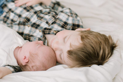 Big brother and newborn baby sister snuggling on bed