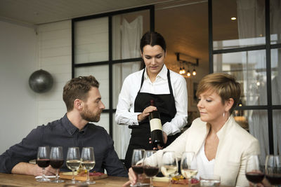 Woman wearing apron showing wine bottle to business people at table