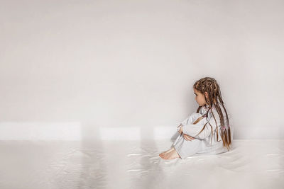 Girl with braided hair sitting on bed against white wall