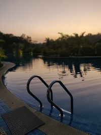 Swimming pool by lake against sky during sunset