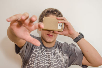 Smiling teenager boy covering eyes with smart phone in cardboard box