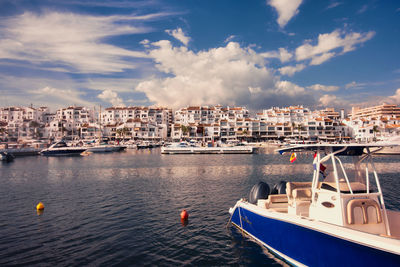 Sailboats moored in sea by buildings against sky