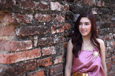 Portrait of smiling young woman standing against brick wall