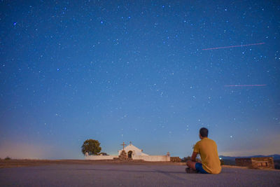 Rear view of man sitting against clear sky at night