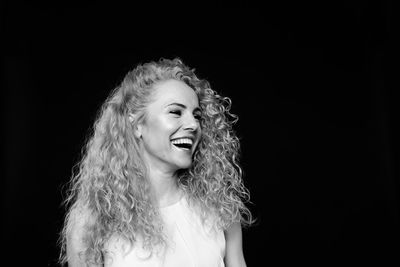 Happy woman with curly hair standing against black background