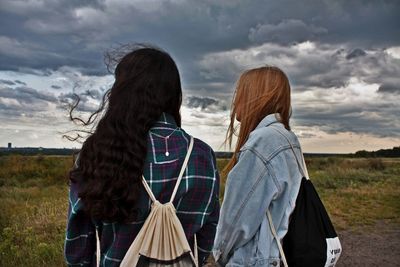 Rear view of women standing on field against sky