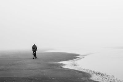 Rear view of man riding bicycle at beach during foggy weather