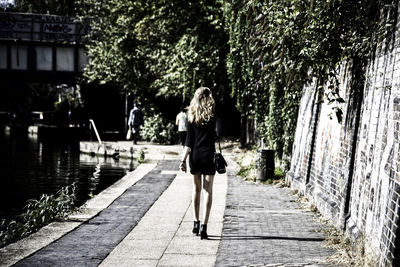 Rear view of woman walking on footpath by canal