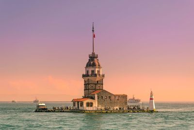 Lighthouse in sea against sky during sunset