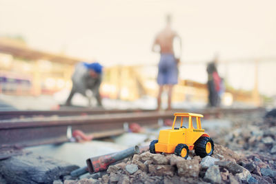 Close-up of toy with people working on railroad track against sky