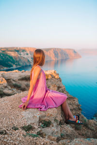 Rear view of woman sitting on rock against sky