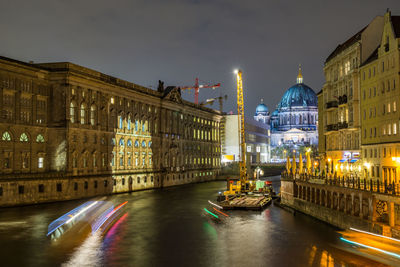 Light trails on canal by illuminated berlin cathedral against sky at night