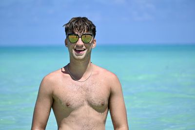 Portrait of shirtless man wearing sunglasses standing at beach