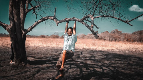 Full length portrait of woman standing on tree trunk