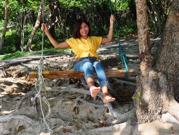 Portrait of smiling woman sitting on swing hanging from tree trunk