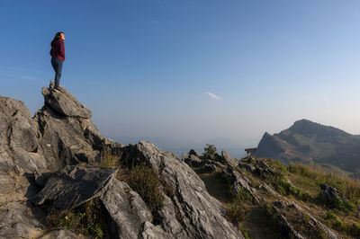 Man standing on rock by mountain against sky