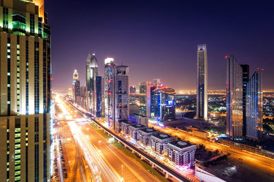 Light trails of dubai downtown skyline by buildings against sky at night