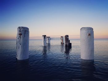 Wooden posts in sea against sky during sunset