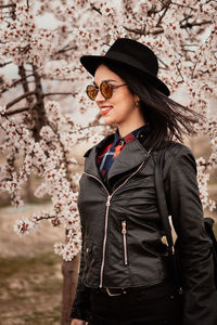 Beautiful woman wearing sunglasses standing against cherry tree