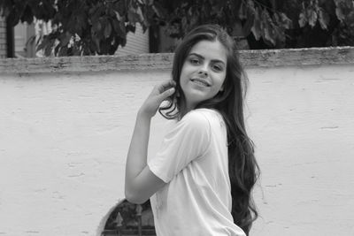 Portrait of smiling young woman standing against wall