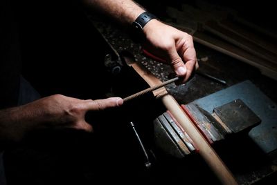 Cropped hands of craftsperson holding metal while working at workshop