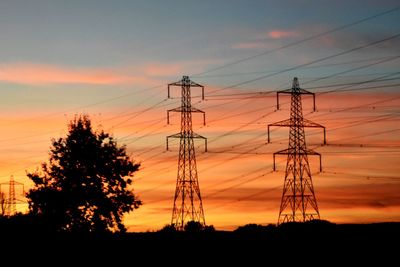 Low angle view of silhouette electricity pylon on field against romantic sky