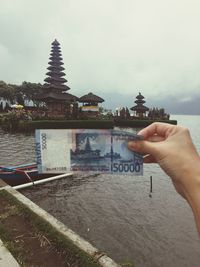 Cropped image of person holding cross in front of temple against sky