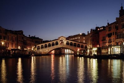 Arch bridge over river by buildings against sky at dusk