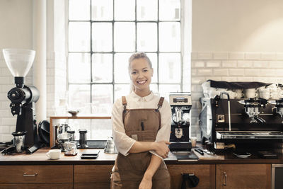 Portrait of happy female barista standing by counter in coffee shop