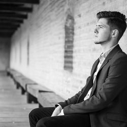 Thoughtful young businessman sitting on seat against wall