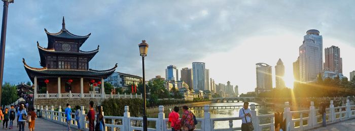 People walking in city against cloudy sky