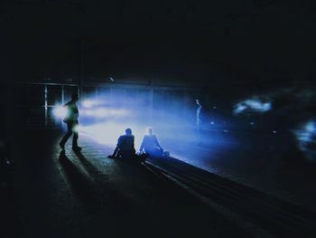 Silhouette people sitting on illuminated road at night