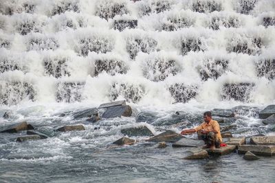 Man sitting on rock against waterfall