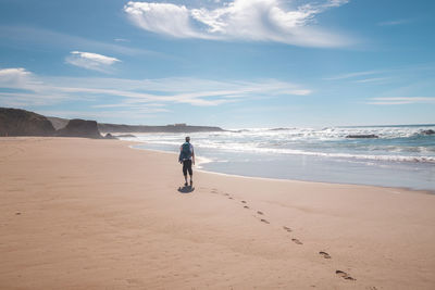 Rear view of woman walking at beach against sky