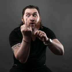 Mid adult man gesturing obscene gesture while sitting against black background